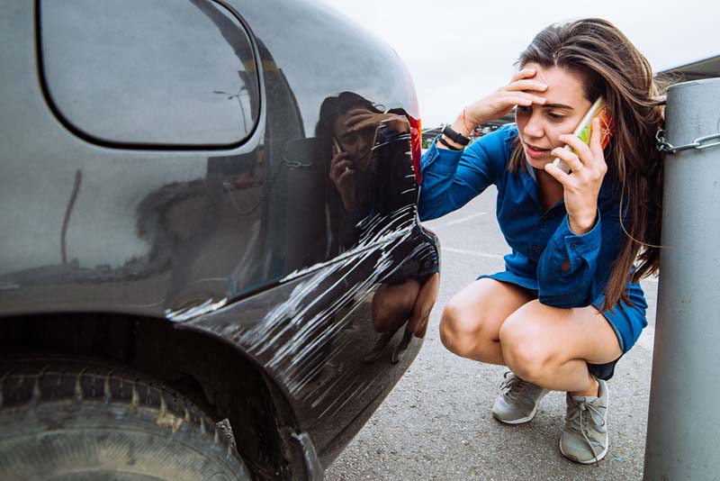 woman calling lawyer after a car accident, damaged car due to accident
